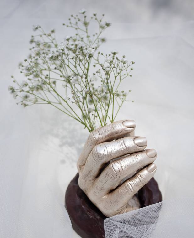 Escultura de una mano en yeso con acabado metálico sosteniendo flores.